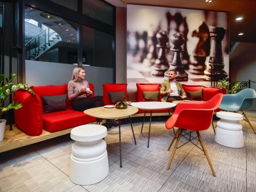 two women sitting in a room with red chairs and tables at ibis Luzern Kriens in Luzern