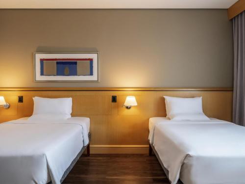 two beds in a hotel room with white sheets at Novotel Sao Paulo Center Norte in Sao Paulo