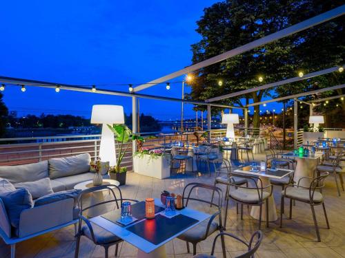 a patio with tables and chairs at night at Novotel Szeged in Szeged