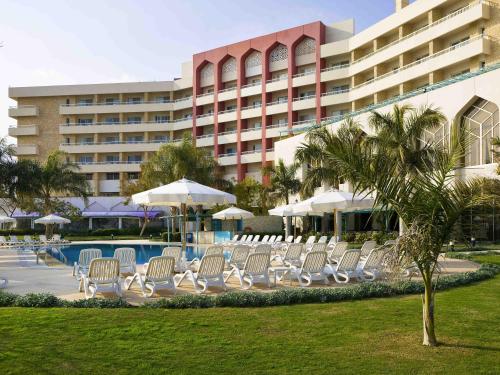 a group of chairs and umbrellas in front of a hotel at Mercure Ismailia Forsan Island in Ismailia
