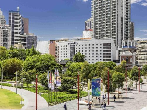 a city with people walking around a park with tall buildings at Novotel Sydney Darling Square in Sydney