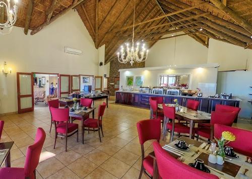 a restaurant with tables and red chairs and a kitchen at Piekenierskloof Mountain Resort by Dream Resorts in Citrusdal
