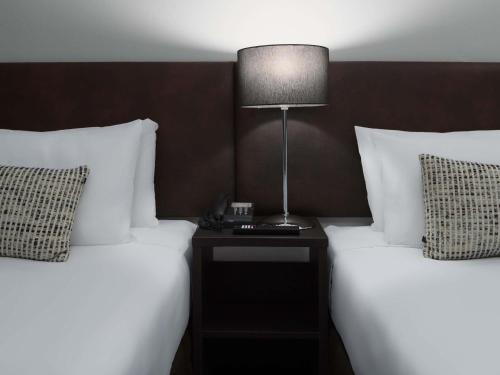 two beds with white sheets and a lamp on a night stand at Mercure Welcome Melbourne in Melbourne