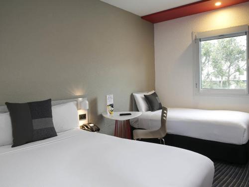 a hotel room with two beds and a table and a window at ibis Sydney Airport in Sydney