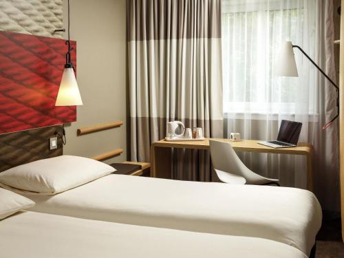 a hotel room with a bed and a desk with a laptop at ibis London Stratford in London