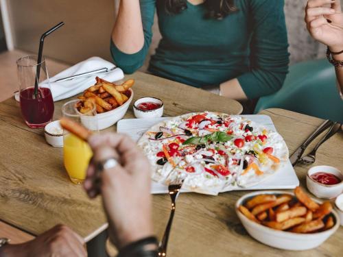 a group of people sitting at a table with a pizza and fries at ibis London Stratford in London