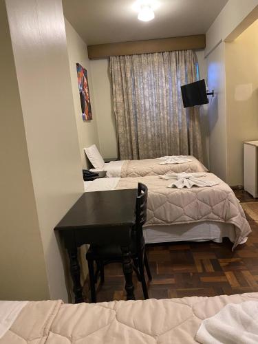 a room with two beds and a table and a desk at Hotel Ponta Grossa São Marcos in Ponta Grossa