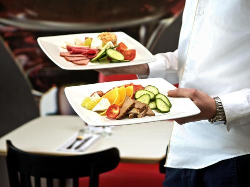 a chef holding two plates of food on a table at Ibis Warszawa Ostrobramska in Warsaw