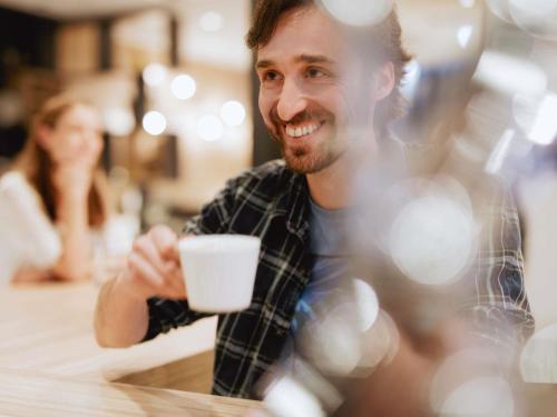 a man sitting at a table holding a cup of coffee at Ibis Warszawa Ostrobramska in Warsaw
