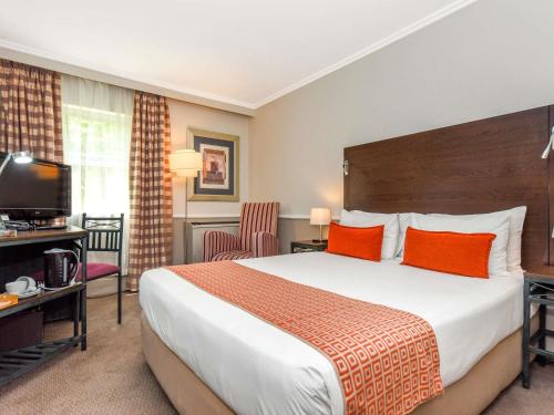 una camera d'albergo con un grande letto con cuscini arancioni di Mercure Johannesburg Randburg a Johannesburg
