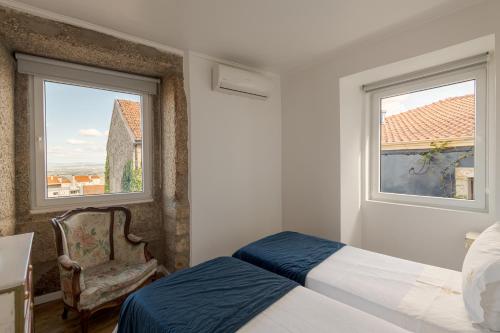 a bedroom with a bed and a chair and two windows at Memórias Charme Residences in Covilhã