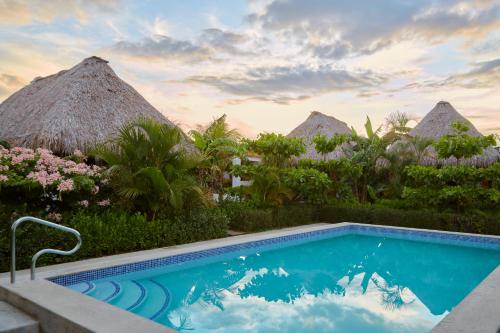 a swimming pool in front of a resort with thatch huts at Banana Tree Popoyo in Popoyo
