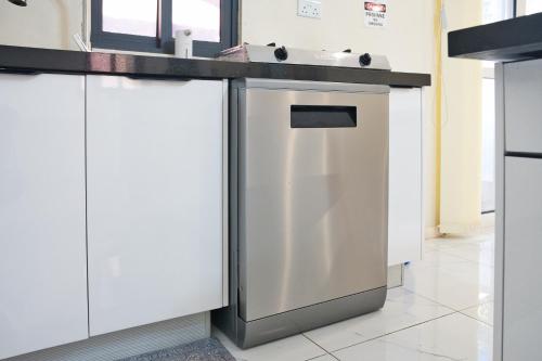 a kitchen with white cabinets and a stainless steel dishwasher at The Emerald Apartments Ibex Meanwood in Lusaka