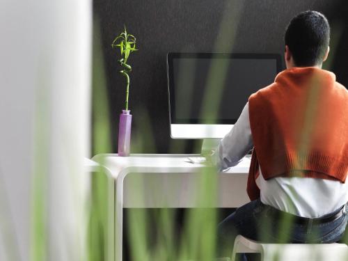 a man sitting at a desk with a computer with a plant at Novotel Leuven Centrum in Leuven
