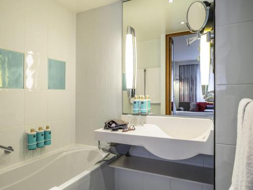 a white bathroom with a tub and a sink at Novotel Mechelen Centrum in Mechelen