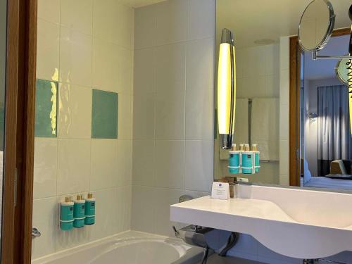 a bathroom with a tub and a sink and a mirror at Novotel Mechelen Centrum in Mechelen