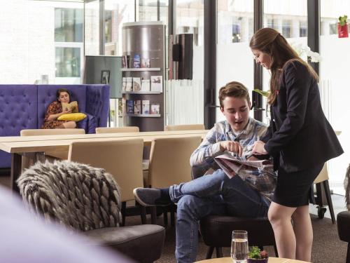 a woman standing next to a man sitting in a chair at Novotel Mechelen Centrum in Mechelen