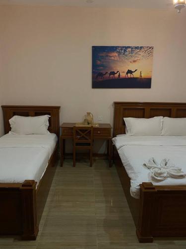 a bedroom with two beds and a desk and a painting at Durrat Nizwa Inn in Nizwa