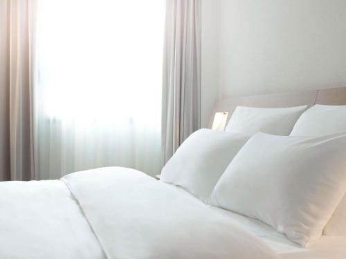 a white bed with white pillows in front of a window at Novotel Lille Centre Gares in Lille