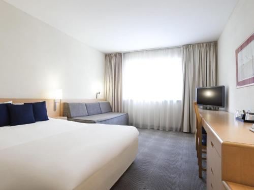 a hotel room with a large bed and a television at Novotel Ieper Centrum in Ypres