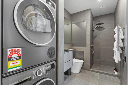 a bathroom with a washer and dryer next to a toilet at QV Stays Modern City Retreat in Auckland