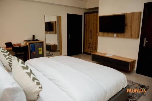 a bedroom with a white bed and a flat screen tv at Momo's Guest House in Kumasi