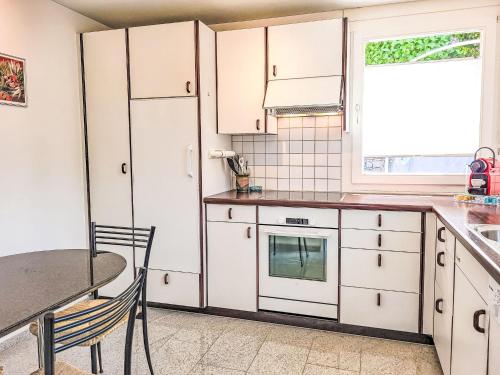 Monte CeneriにあるApartment La Perla by Interhomeの白いキャビネットとテーブルと窓のあるキッチン