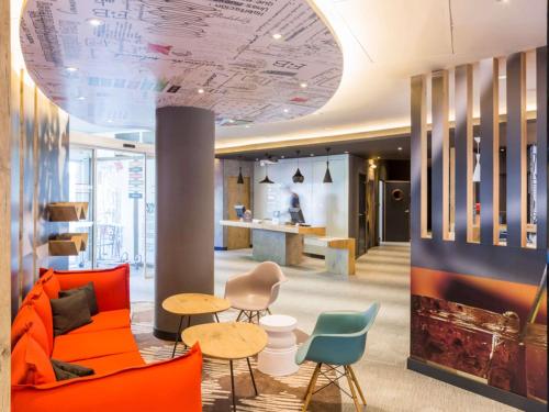 an office lobby with a orange couch and chairs at Ibis Barcelona Castelldefels in Castelldefels