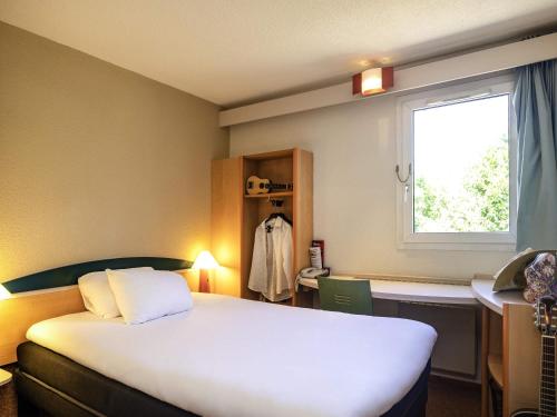a hotel room with a bed and a window at Hotel ibis Autun in Autun