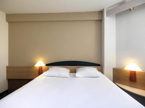 a bedroom with a large white bed with two lamps at Hotel ibis Autun in Autun