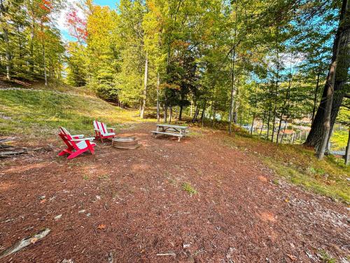 two red chairs and a picnic table in the woods at Blue Lake Cottage - 10 Minutes to Minocqua in Minocqua