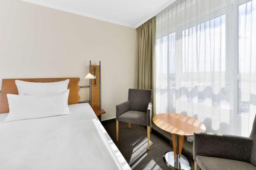 a hotel room with a bed and a chair and a window at NH Mannheim Viernheim in Viernheim
