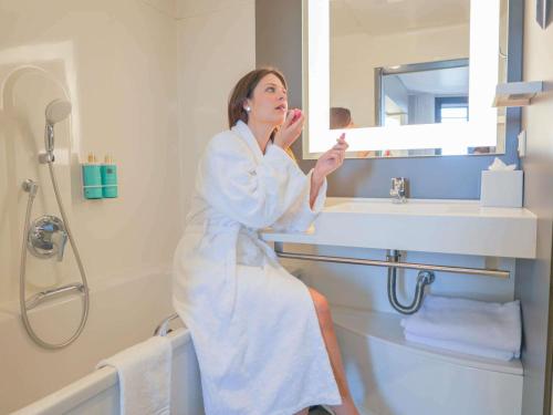 a woman sitting in a bathroom brushing her teeth at Novotel Suites Paris Montreuil Vincennes in Paris