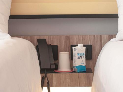 a shelf between two beds with a bottle of water and a phone at Ibis Monterrey Aeropuerto in Monterrey