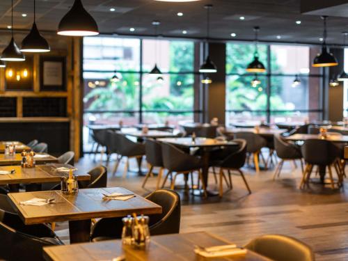 a restaurant with wooden tables and chairs and windows at Novotel Leeds Centre in Leeds