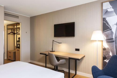 a hotel room with a desk and a tv on a wall at NH München Airport in Oberding