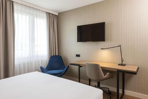 a hotel room with a desk and a bed and a television at NH München Airport in Oberding