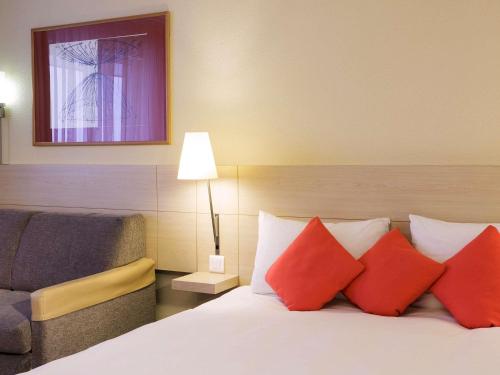 a bedroom with a bed with red pillows and a chair at Novotel Milton Keynes in Milton Keynes