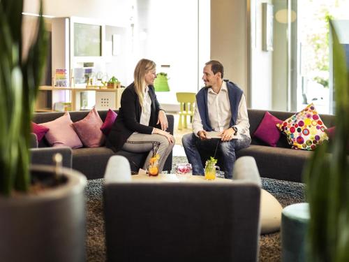 a man and woman sitting on couches in a living room at Novotel Düsseldorf City West in Düsseldorf