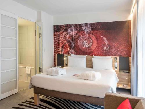 a bedroom with a large white bed with a painting on the wall at Novotel München City in Munich