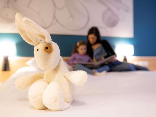 a stuffed rabbit sitting on a bed with a woman at ibis Besançon Centre la City in Besançon