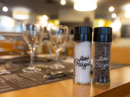 two salt and pepper bottles on a table with wine glasses at ibis Besançon Centre la City in Besançon