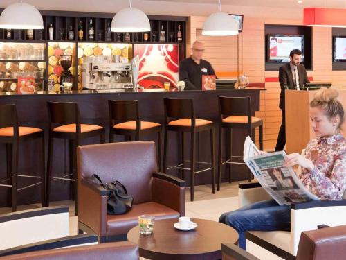 a woman sitting in a chair reading a newspaper in a bar at Ibis Barcelona Mollet in Mollet del Vallès