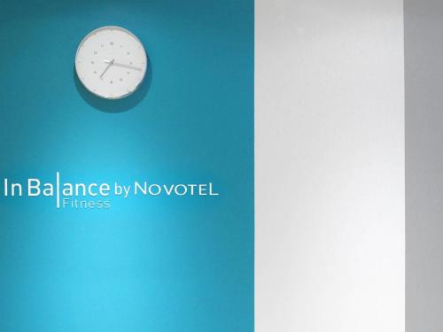 a clock on a blue wall with the words in ballance by novel at Novotel Suites Paris CDG Airport Villepinte in Roissy-en-France