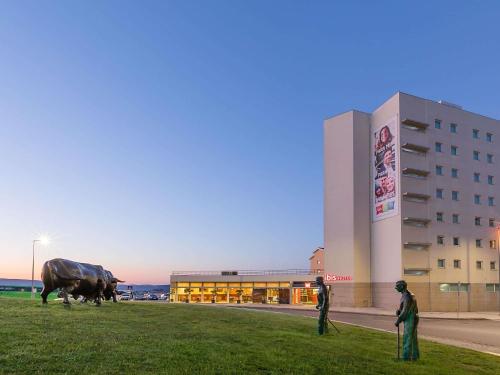 two people standing in front of a building with a statue of a cow at Hotel ibis Bragança in Bragança