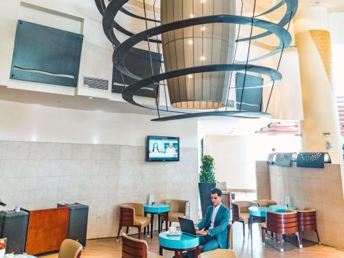 a man sitting at a table in a restaurant with a laptop at Novotel Cairo 6th Of October in 6th Of October