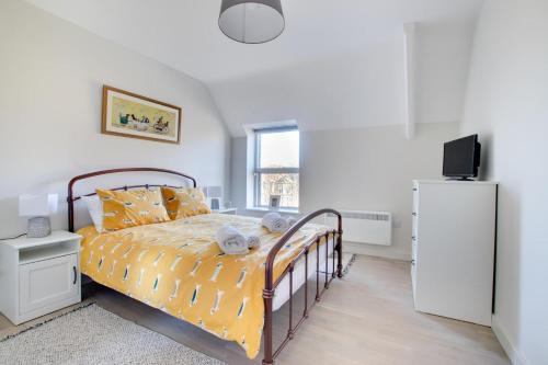 a bedroom with a bed with yellow sheets and a refrigerator at Daisy’s - Ellinbrook Apartments in Hunstanton