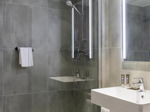 a bathroom with a shower with a sink and a mirror at Novotel Szczecin Centrum in Szczecin