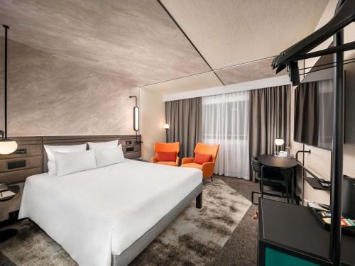 a hotel room with a white bed and orange chairs at Novotel Warszawa Centrum in Warsaw