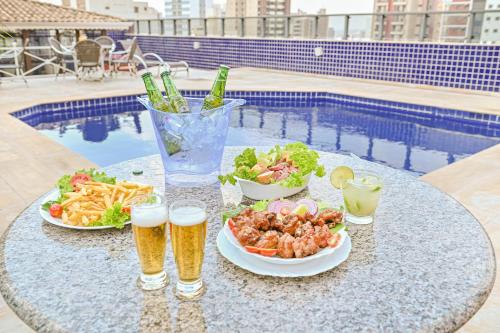 a table with two glasses of beer and plates of food at Hotel Dan Inn Campinas Cambuí - Um Hotel Clássico em Campinas By Nacional Inn in Campinas
